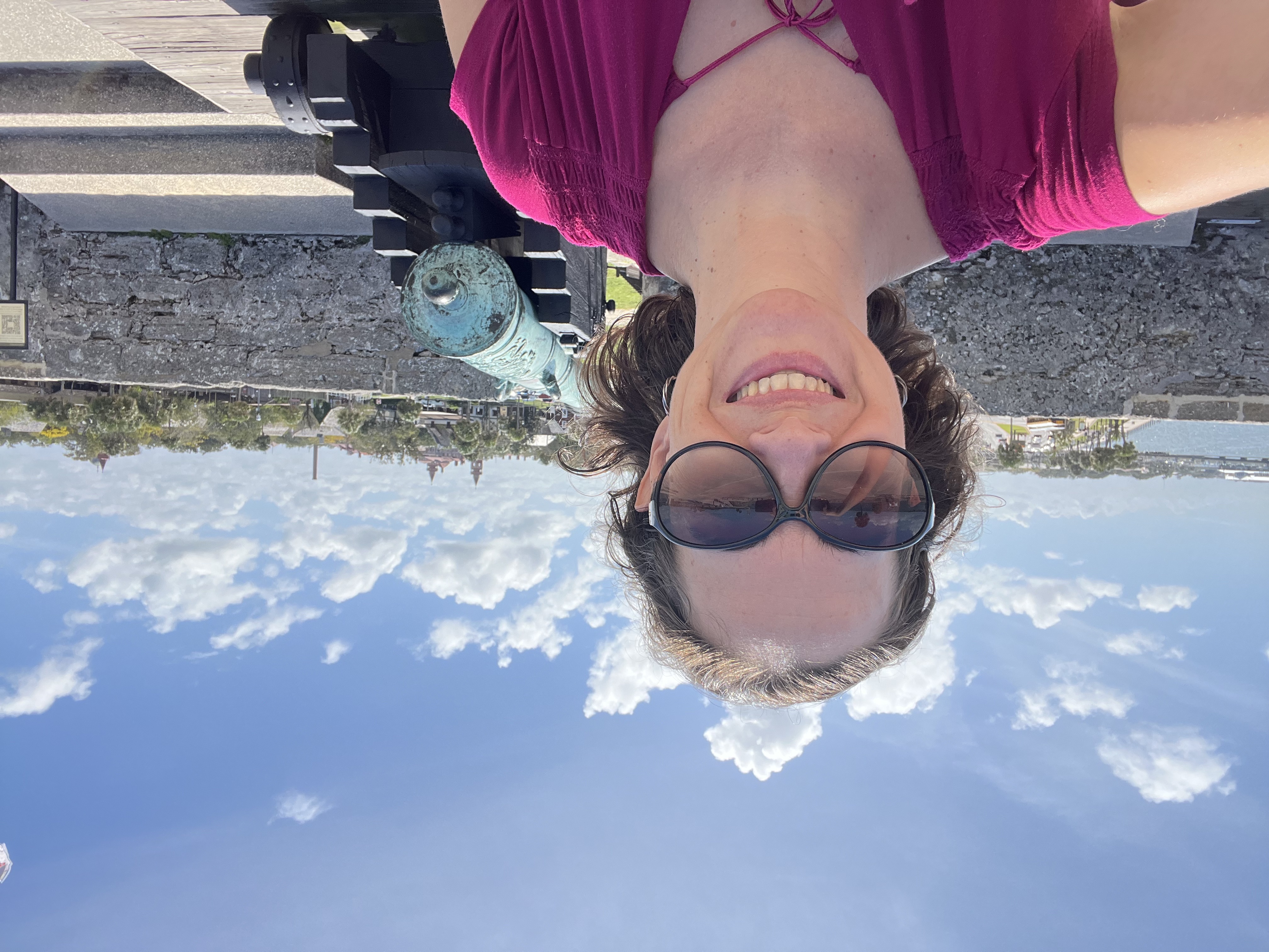 A woman with sunglasses taking a selfie with blue sky and puffy white clouds on a sunny day